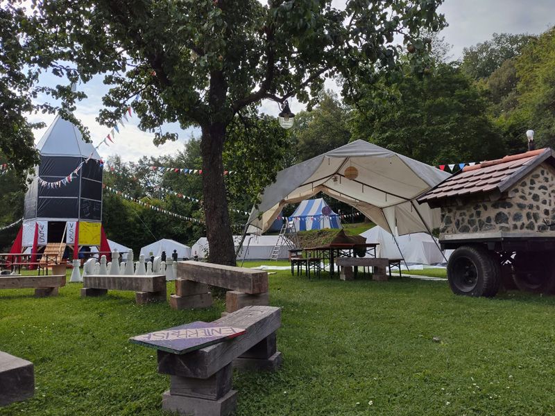 Ein großes Zelt mit Tisch und Stühlen, umgeben von grünem Gras, bietet Platz für gesellige Zusammenkünfte.