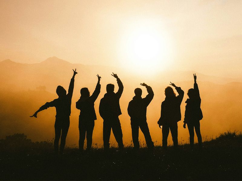Silhouette einer Gruppe von Menschen, die bei Sonnenuntergang auf einem Berg stehen und die Aussicht genießen.